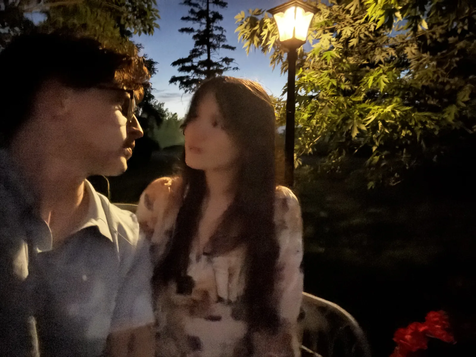 Two people looking at each other at dusk under a lit lamp post, a soft out-of-focus shot